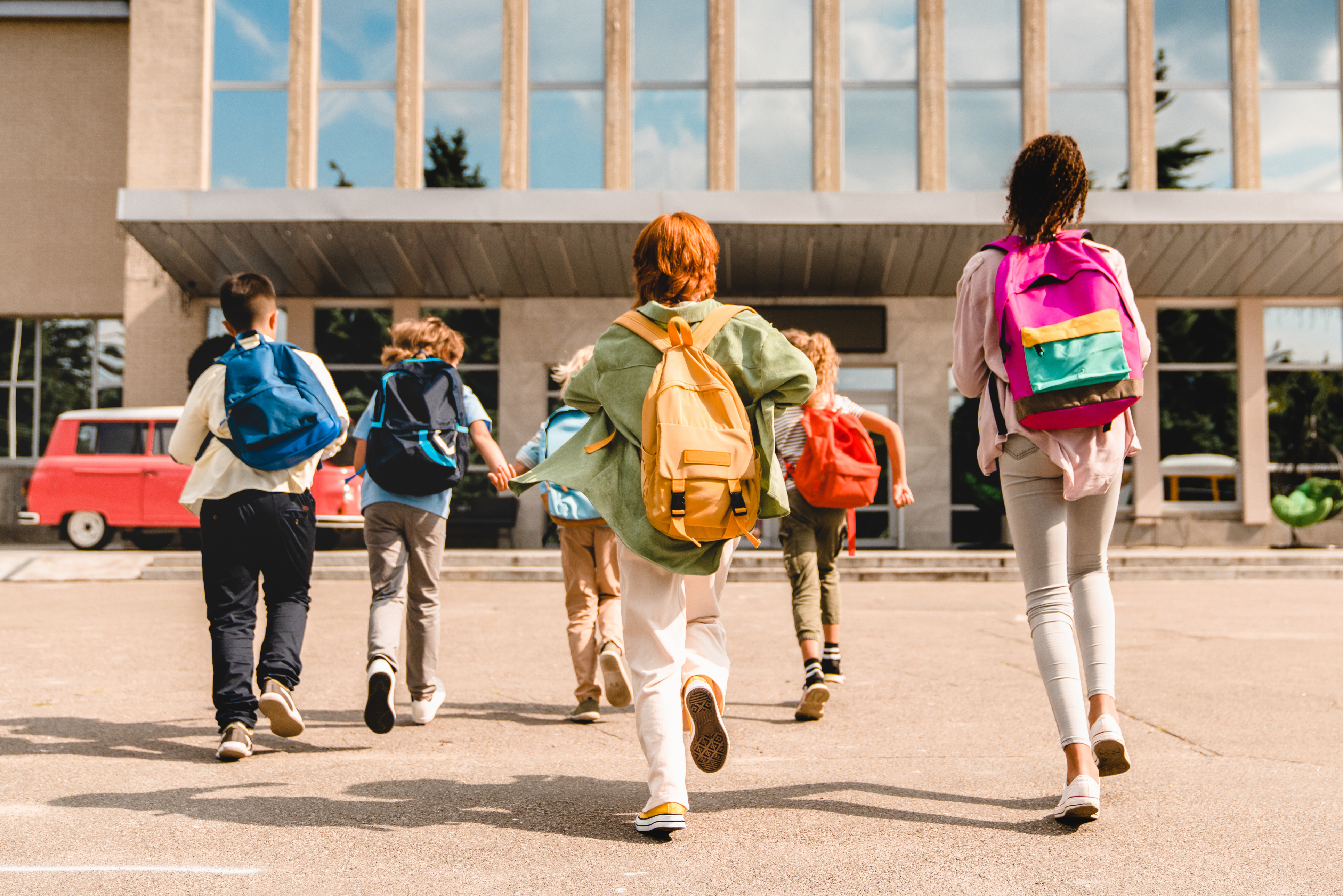 Diverse group of kids running towards school with backpacks.