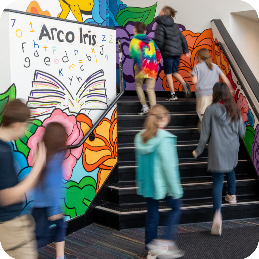 Students running up stairs inside a school with a colorful rainbow mural.