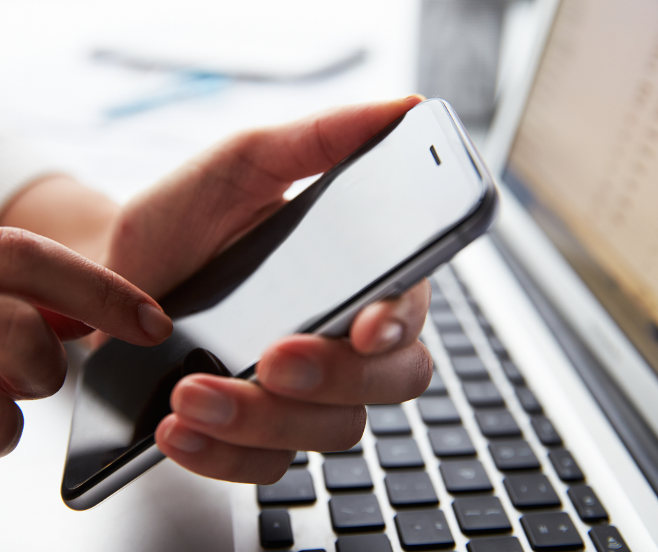 a person holds a mobile phone near a laptop computer