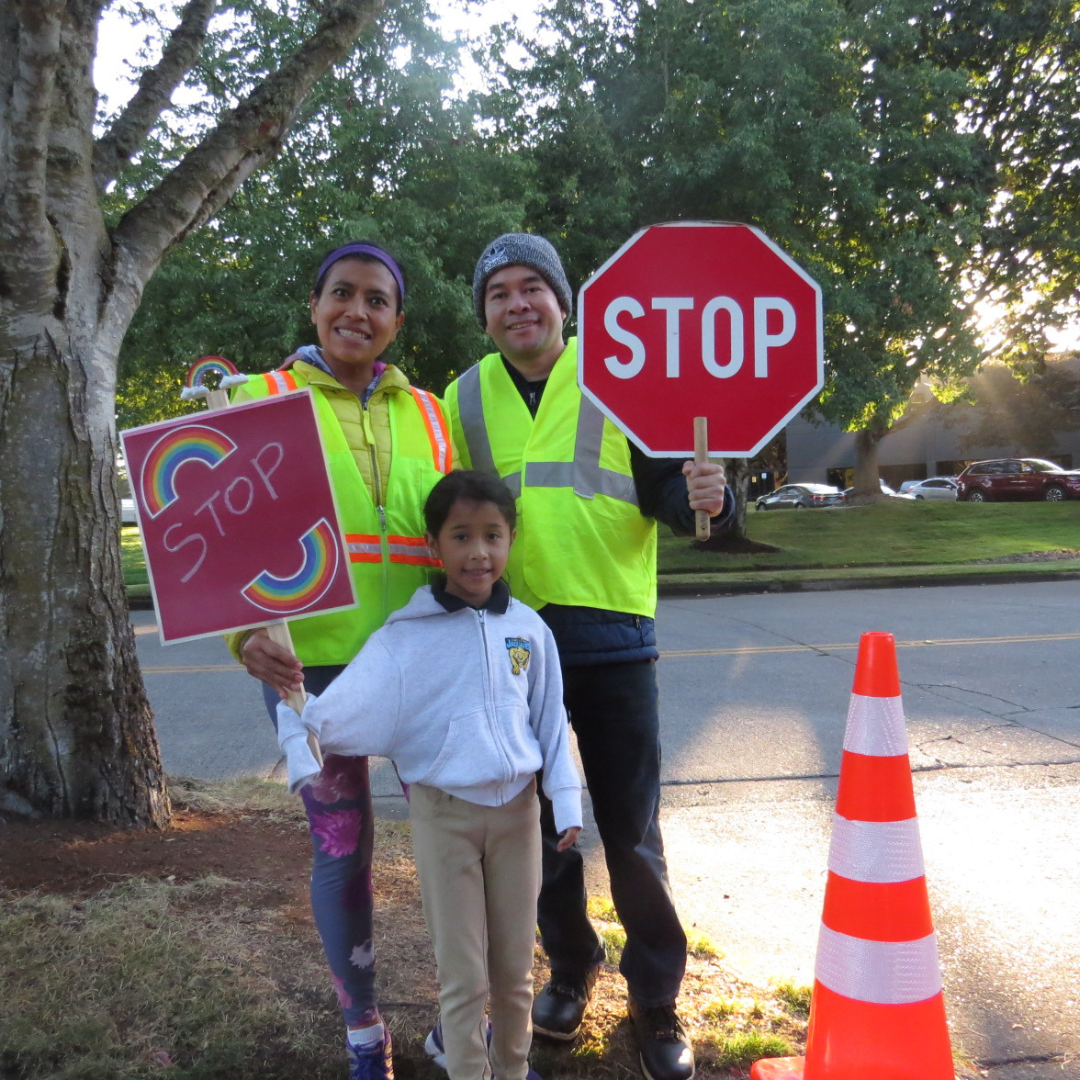 A family holds stop signs while performing crossing guard duty.