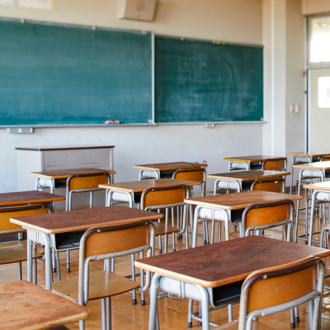 empty desks in a classroom with a blank chalkboard