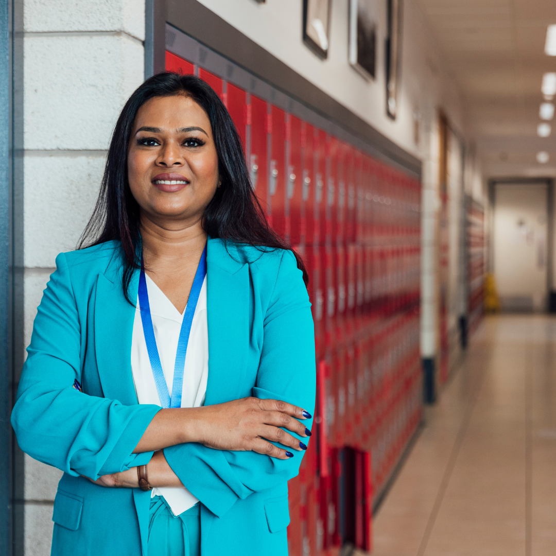 A school leader stands in a hallway with lockers behind her.