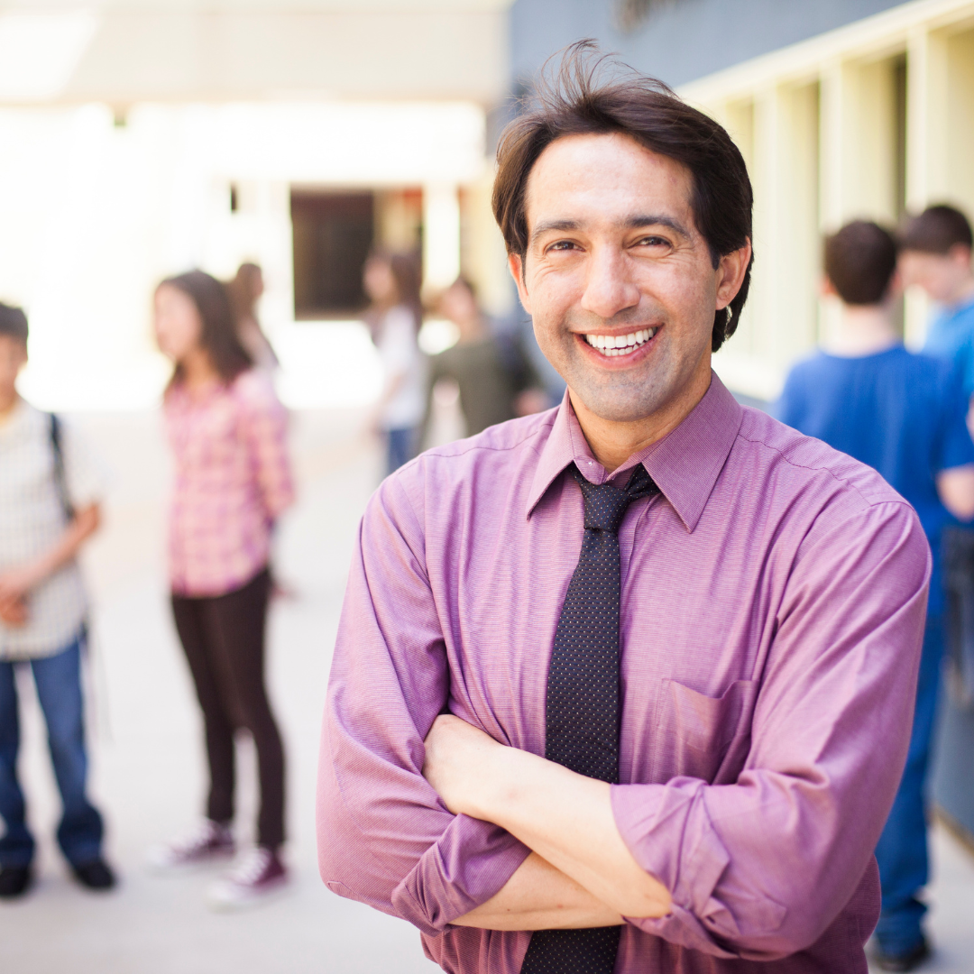 principal stands outside a school building with students in the background
